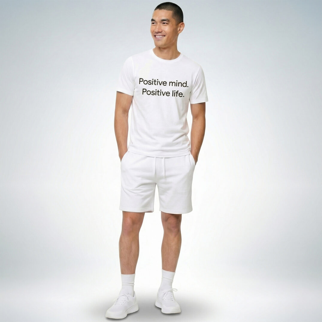 Männliches Model trägt weißes T-Shirt mit „Positive mind. Positive life.“ Print und weiße Shorts im cleanen Sommer-Look – Sinnstoff