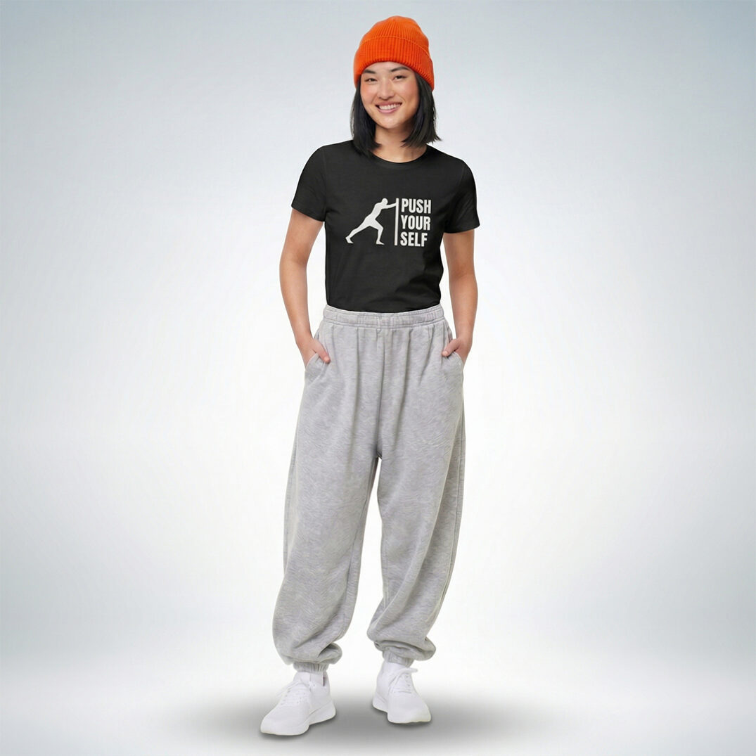 Weibliches Model mit orangefarbener Mütze trägt schwarzes T-Shirt mit „Push yourself“ Print und graue Jogginghose im sportlich-lässigen Look – Sinnstoff