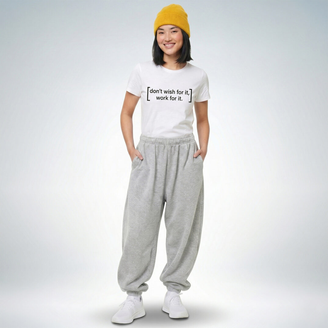 Eine lächelnde Person trägt ein weißes T-Shirt mit dem Schriftzug „don’t wish for it, work for it“, kombiniert mit grauen Jogginghosen und einer gelben Mütze – ein sportlich-entspannter Look mit motivierender Botschaft.