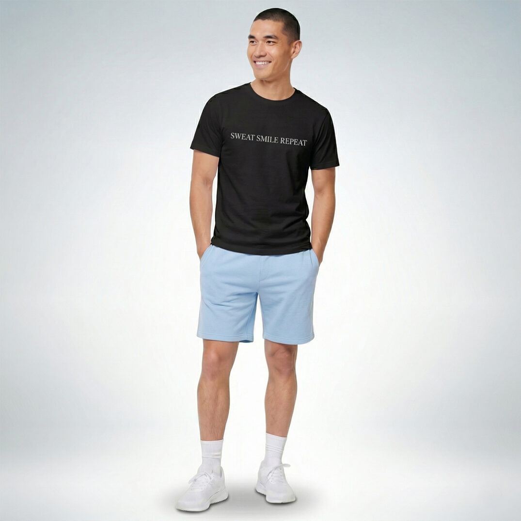 Ein männliches Model präsentiert ein schwarzes T-Shirt mit der Aufschrift „Sweat Smile Repeat“ und hellblauen Shorts – Sinnstoff.