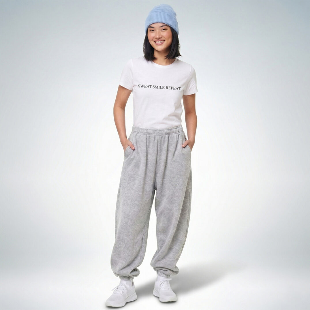 Ein weibliches Model präsentiert ein weißes T-Shirt mit der Aufschrift „Sweat Smile Repeat“ und grauer Jogginghose – Sinnstoff.